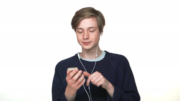 Portrait of Glad Thin Teenage Boy in Braces Choosing His Favourire Song on Smartphone Enjoying Music