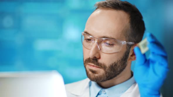 Enthusiastic Male Cyber Science Researcher Looking at Screen of Laptop Holding Microchip Processor