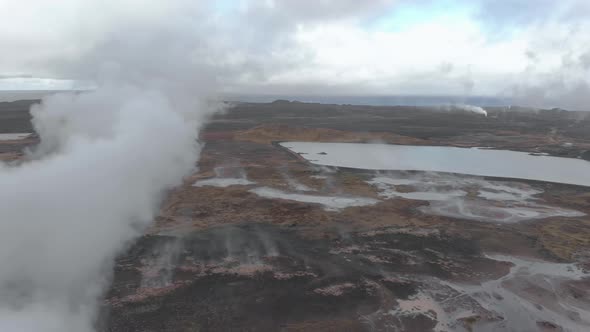 Aerial panning shot of a geothermal hot spring billowing steam from the ground.