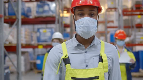 African Worker in Safety Helmet Wearing Face Protective Medical Mask Inspecting Warehouse