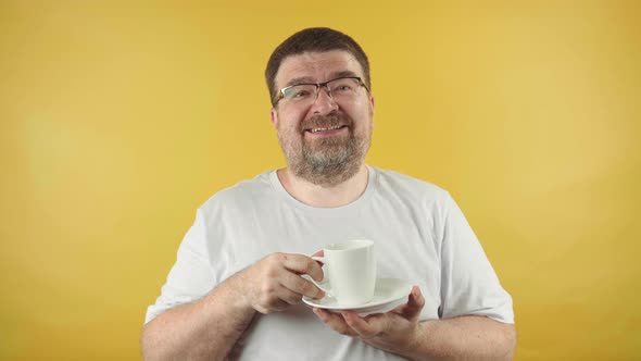 European caucasian man with a beard and glasses is man drinks hot coffee or tea, feeling happy.