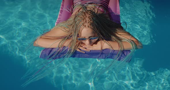 Top View A Child with Afro Pigtails Swims on an Inflatable Mattress in the Pool Resting and Enjoying