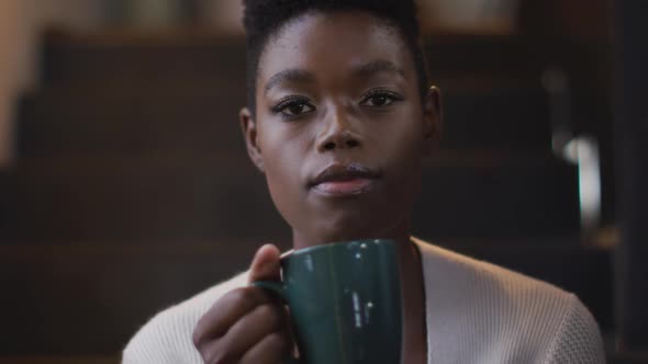 Portrait of smiling african american attractive woman sitting on stairs an, drinking coffee