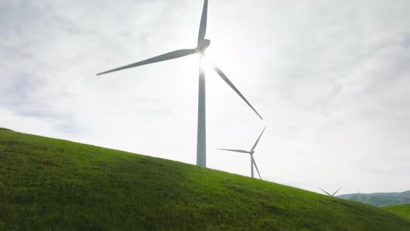 Drone Flying Low Above Grasslands to Windmill on Top Green Hill at Cloudy Sunset