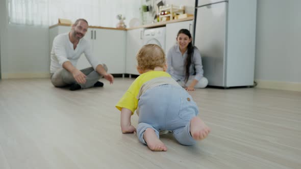 Caucasian baby boy child crawling with parents support in house to develop skill in living room.