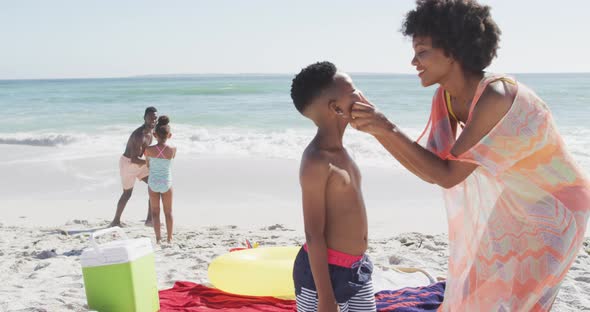 Smiling african american family using sun cream on sunny beach