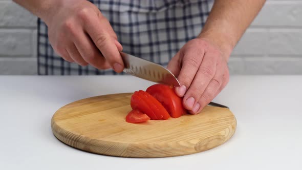 Man's hand slicing red fresh tomatoes on a cutting board.