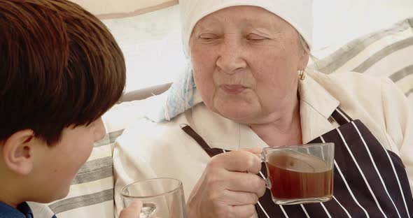 Grandson and Grandmother are Drinking Tea While Sitting on a Garden Swing