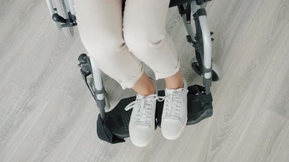 High Angle View of Female Feet of Paraplegic Woman Sitting in Wheelchair Indoors