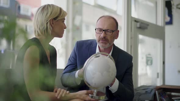 Businessman and woman during meeting in coffee shop, looking at globe