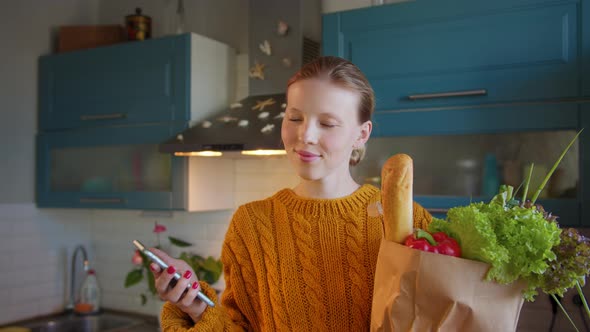 Young Woman with Groceries Bag in Hands Kitchen Shows Phone Green Screen