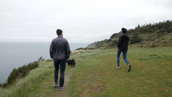 Couple walks along a bluff overlooking the Pacific Ocean with the dog.