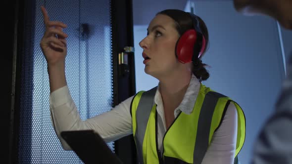 Diverse female and male it technicians wearing headphones using tablet checking computer server