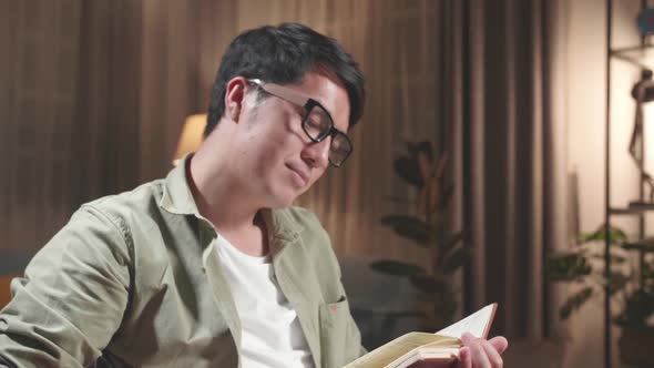 Asian Man Sitting In A Wheelchair And Reading Book At Home