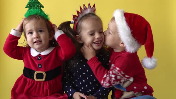 Emotion Cute Happy 3 Siblings Friends Baby Girl And Boy Kissing in Santa Suit Looking On Camera At