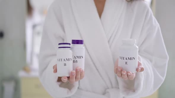 Unrecognizable Slim Caucasian Woman Holding Bottles of Vitamin D3 E and B Standing in Bathroom at