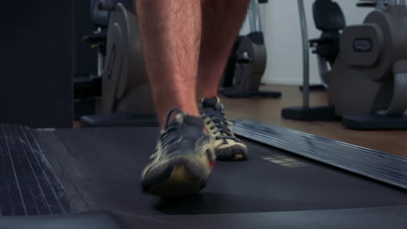 A Fit Man Walks on a Treadmill in a Gym - Front Closeup on the Feet