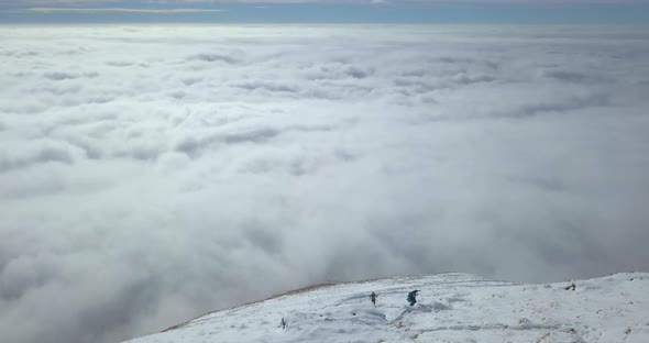 Aerial drone view of men hiking in the clouds and snow covered mountains in the winter.