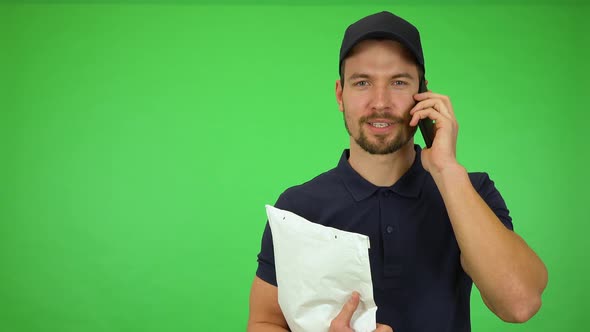 A Young Handsome Mailman Talks on a Smartphone While Smiling at the Camera - Green Screen Studio