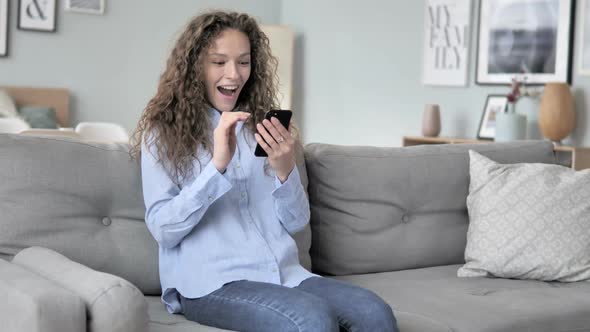 Curly Hair Woman Cheering Success on Smartphone While Sitting on Couch