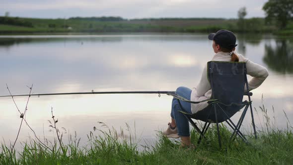 Woman with a Fishing Rod Sitting on a Chair By the Lake