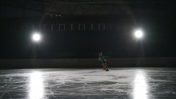 Junior Single Female Figure Skater is Training on Ice Rink Exercising Jump and Camel Spin Warmup