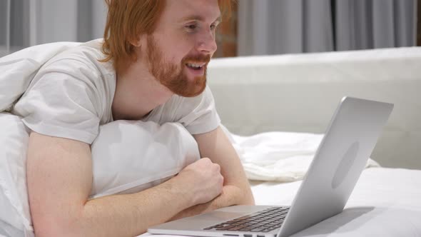 Online Video Chat by Excited Man Lying on Stomach in Bed