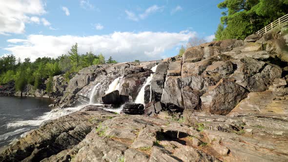 Cascading waterfall flows down rock face into lake basin on bright sunny day in Muskoka Ontario