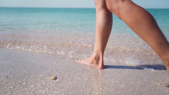 Slim Girl Legs Walking Along the Sandy Beach Along the Transparent Turquoise Sea