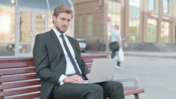 Thumbs Down By Young Businessman with Laptop Sitting on Bench