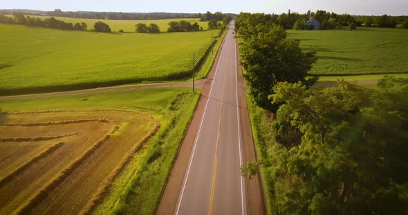 Aerial of cars driving down a road in a picturesque countryside on an idyllic August morning.