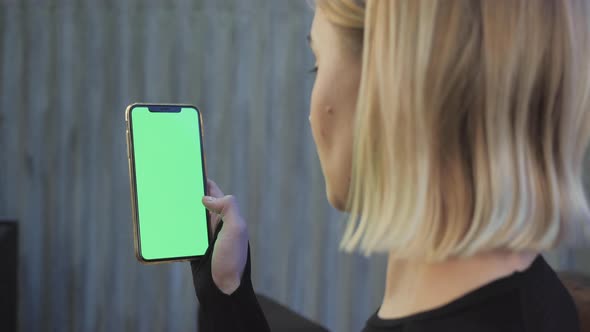 A Young Athletic Woman Holds A Smartphone in Her Hand, Shows A Green Chromakey Screen, Is in The Gym