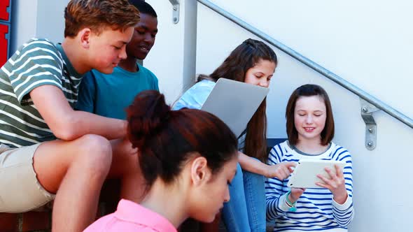 Group of smiling school friends on staircase using laptop and digital tablet