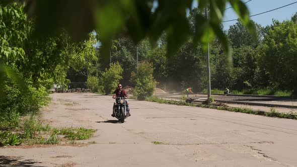 Man Without Helmet Wearing Black Glasses Rides Motorcycle Forward Along Asphalt Road Between Trees