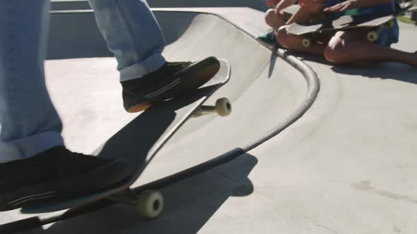 Laughing caucasian woman and man sitting, looking at skateboarding friend on sunny day