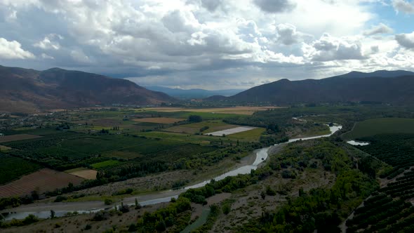 Aerial orbit of green farm fields and stream river, mountains in background on a cloudy day, Cachapo