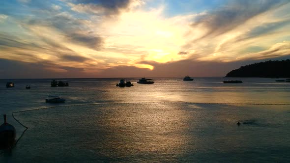 An aerial, beautiful colour wide shot of an ocean while sun is setting with boats and waves on the f