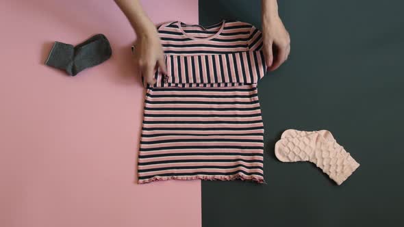 Woman Hands Stack Kid Clothes on Two Colored Grey Pink Background