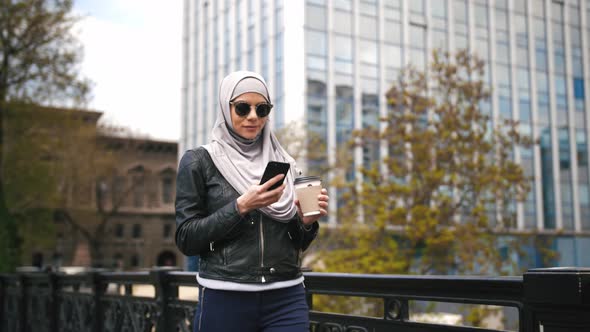 Portrait of Young Stylish Muslim Business Woman in Hijab and Sunglasses Walking Outdoors with Cup of