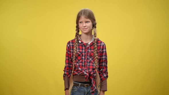 Medium Shot Teenage Caucasian Girl with Long Pigtails Standing at Yellow Background Looking Around