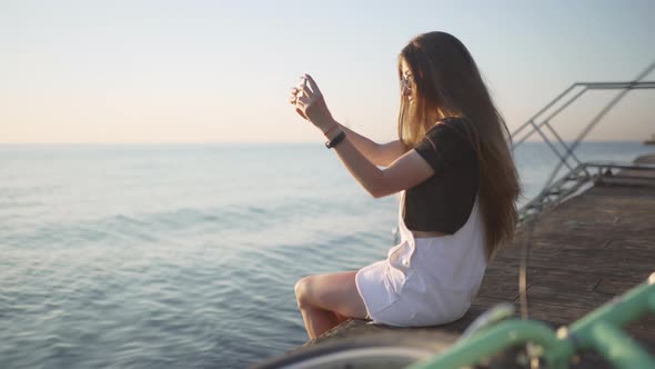 Young Attractive Woman Taking Pictures of Sea at Sunset or Sunrise