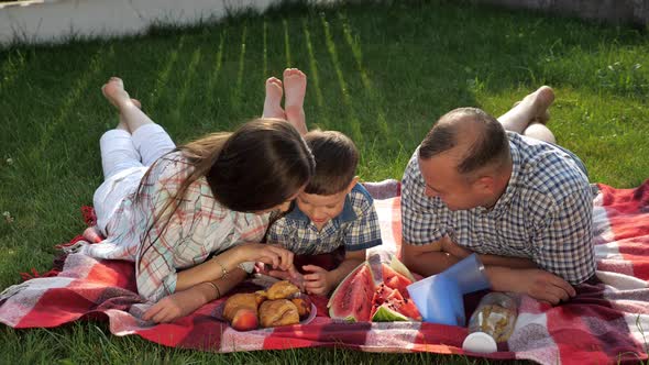 Happy Family Members Lie on Stomach on Red Blanket at Picnic