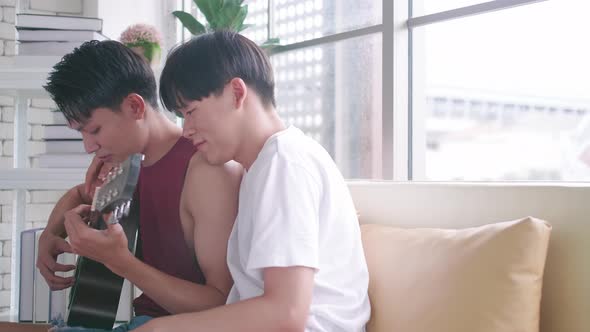 Happy gay Asian couple spending time together on sofa at home.