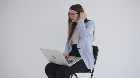 Confident Young Business Woman with Glasses Works on a Laptop While Sitting on a Chair and