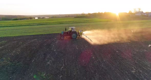 Tractor with trailed sprayer spraying chemicals on agricultural field. Aerial view.