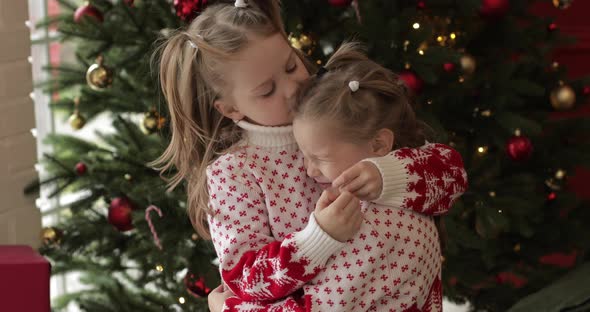 Happy Small Girls in Warm Sweaters and Beautiful Hairstyles on Christmas Eve at Home