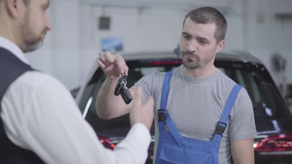 Portrait of Young Caucasian Workman Returning Car Keys To Owner After Warranty Repair