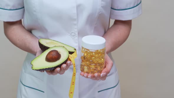 Nutritionist Doctor Holding Organic Avocado Fruit and Jar of Medicine or Vitamin or Omega 3 Capsules