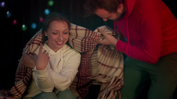 Man Covers Girl with Plaid and Sits Down. Romantic Evening Near Bonfire