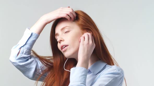 Portrait of Young Redhead Girl Listening To Music Through Headphones on White Background in the